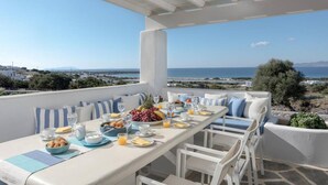 A terrace with a table set for breakfast, overlooking a coastal landscape. - Villa Agali Naxos Glyfada Kastraki (Naxos)