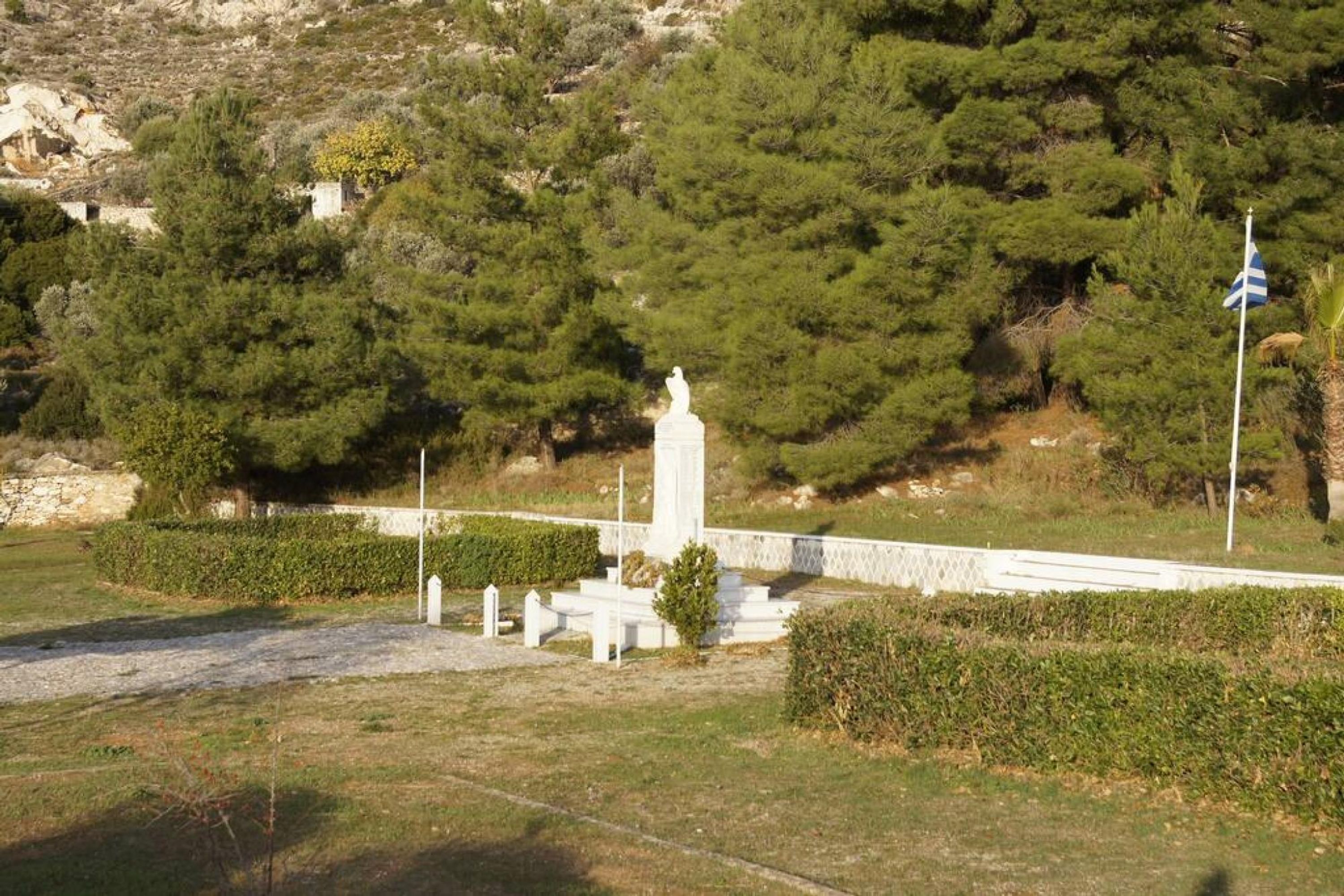 A memorial with a statue, surrounded by neatly trimmed hedges and a flagpole.