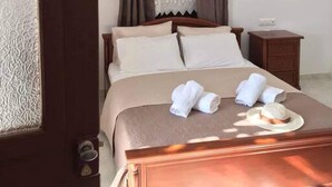 A hotel room with a wooden bed, beige bedding, a nightstand, and a window with curtains. - Giannakis' Filoxenia (Filoti)
