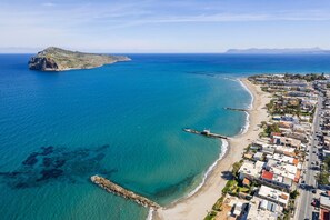 Vista aérea de uma vila costeira com praia, uma ilha rochosa e edifícios residenciais ao longo da costa.