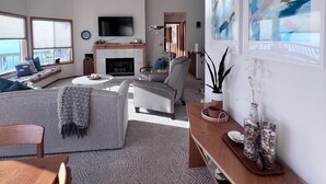 A spacious living room with a fireplace, a large TV, and a view of the outdoors. - Fox Island Beachfront Retreat - Kayaks, Canoe, Paddle Board & Epic Sunsets (Fox Island)