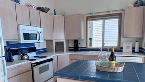 A modern kitchen with light wood cabinets, a white stove, a microwave, and a blue tiled island. - Fox Island Beachfront Retreat - Kayaks, Canoe, Paddle Board & Epic Sunsets (Fox Island)