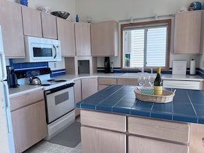 Une cuisine moderne avec des meubles de couleur bois clair, un four blanc, un four à micro-ondes et un îlot central recouvert de carreaux bleus.