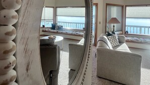 A spacious living room with a large mirror, a sofa, and a view of the ocean through large windows. - Fox Island Beachfront Retreat - Kayaks, Canoe, Paddle Board & Epic Sunsets (Fox Island)