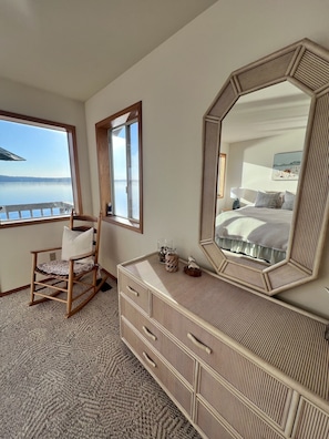 Une chambre avec un grand miroir, un fauteuil à bascule en bois, une commode et une vue sur le lac.