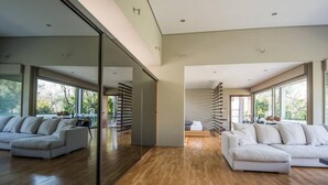 A spacious living room with a large sliding glass door, a wooden floor, and two white sofas. - Studio Rio: Unique space with garden and garage (Ρίο)