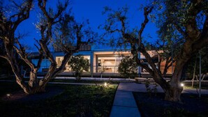 A modern house with a glass facade, surrounded by trees and a pathway. - Studio Rio: Unique space with garden and garage (Ρίο)