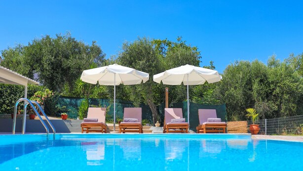Ein Pool mit Liegestühlen und Sonnenschirmen, umgeben von viel Grün.