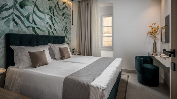 Habitación de hotel moderna con una cama grande, cabecera con diseño de hojas, mesita de noche, escritorio, silla y ventana con cortinas.