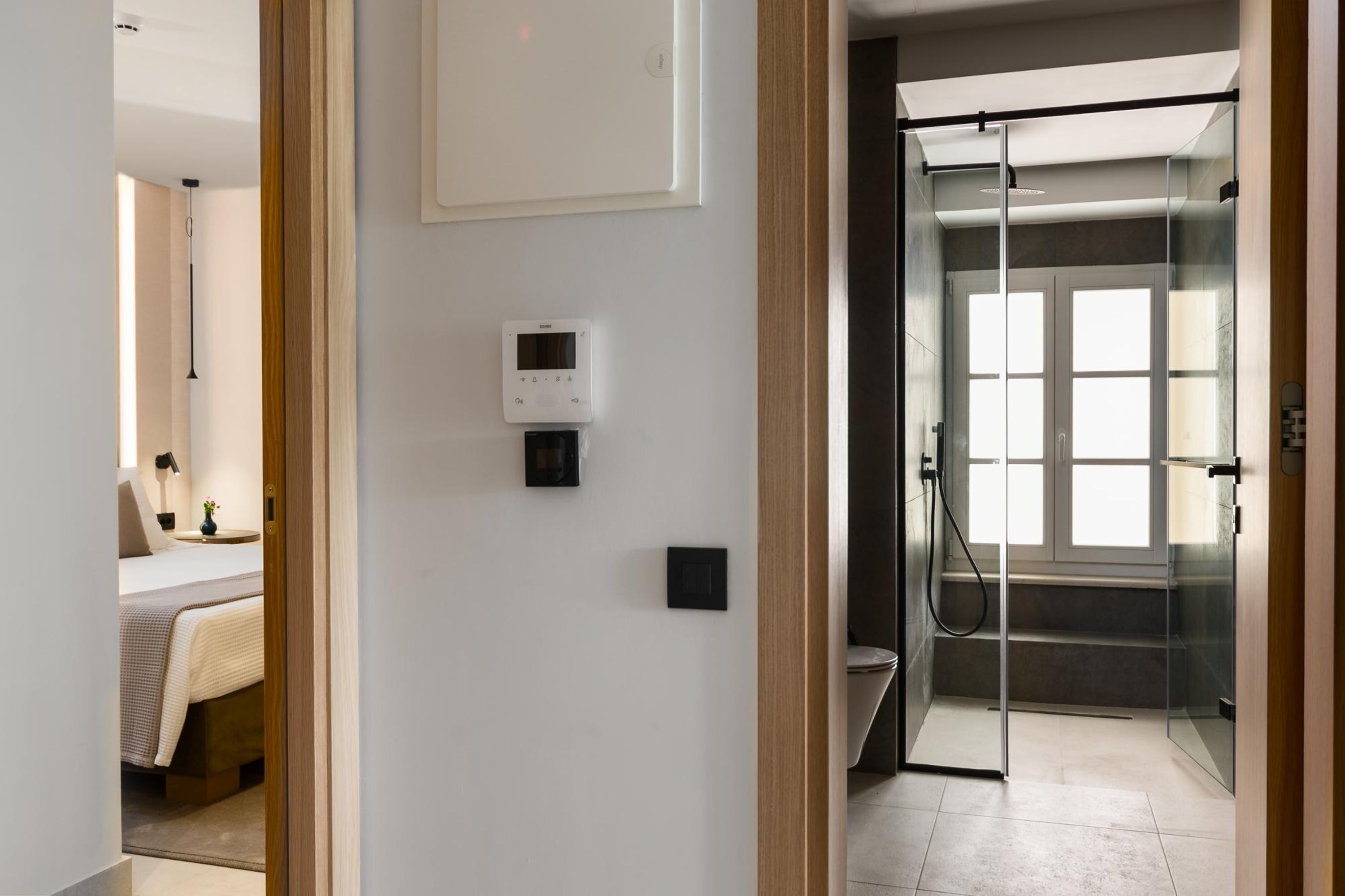 A modern hotel room with a bed, bedside table, and a glass-enclosed shower area.
