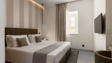 A hotel room with a large bed, a flat-screen TV, a bedside table, and a window with curtains.