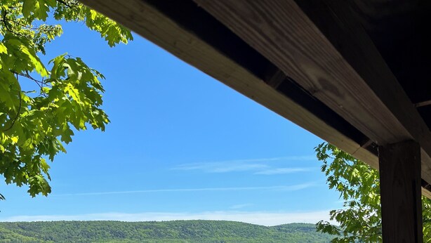 Une terrasse en bois surplombe un lac aux eaux limpides, avec un quai et des collines boisées en arrière-plan.