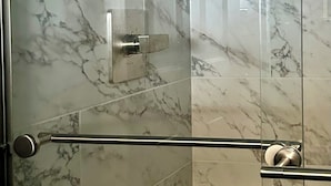 Une salle de bain carrelée de marbre, dotée d’une douche en verre et d’un porte-serviettes en métal.