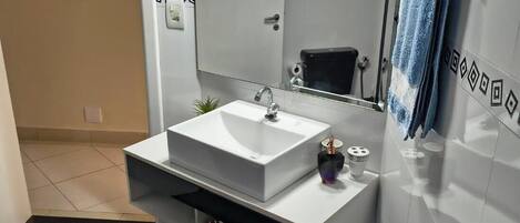 A modern bathroom with a white sink, a large mirror, and a towel rack.