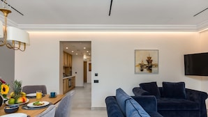 A modern living room with a dark blue sofa, a dining area with a wooden table set for breakfast, and a kitchen in the background. - Penthouse Suite Sea View (Kerkira)