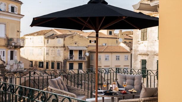A balcony with wicker furniture, a table with wine glasses, and a black umbrella. - Penthouse Suite Sea View (Kerkira)