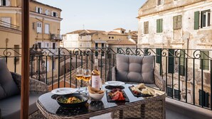 A balcony with a dining table set for two, featuring a bottle of wine, glasses, and a variety of food. - Penthouse Suite Sea View (Kerkira)