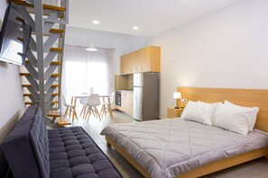 Una moderna camera d'albergo con un letto grande, un divano, un'area pranzo con tavolo e sedie, e un angolo cottura con frigorifero.
