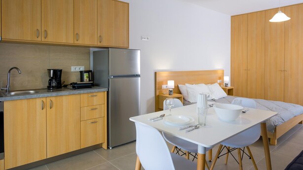 A modern kitchen with wooden cabinets, a stainless steel refrigerator, and a dining area with a white table and chairs. - elounda olithos apartments  6 (Schisma Elountas)