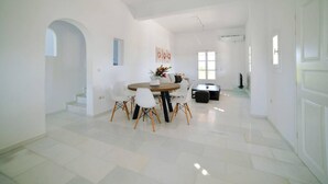 Un comedor amplio y luminoso con una mesa redonda y sillas, una escalera y una puerta que da a otra habitación.