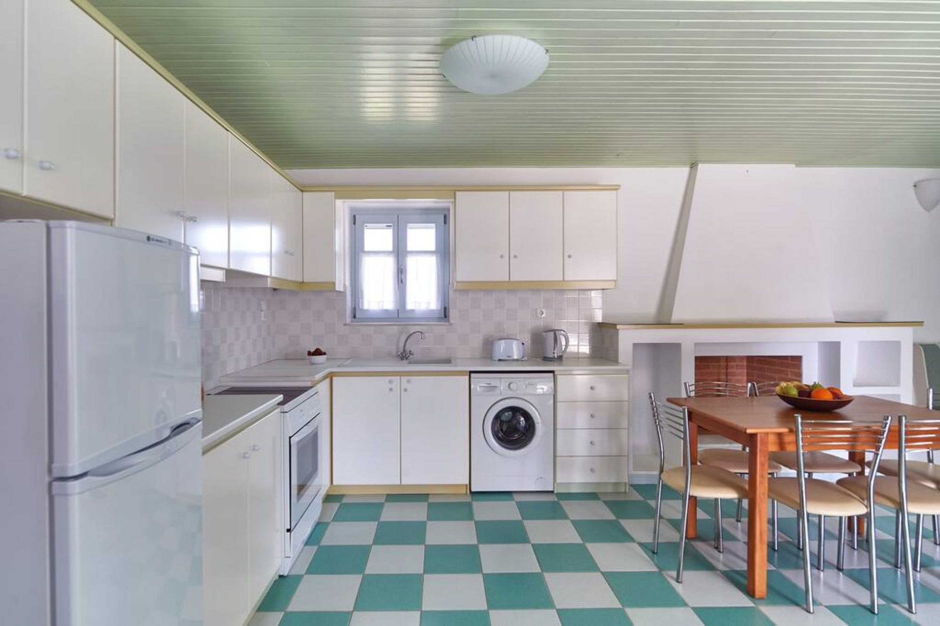 A compact kitchen with a washing machine, a refrigerator, and a dining area with a table and chairs.