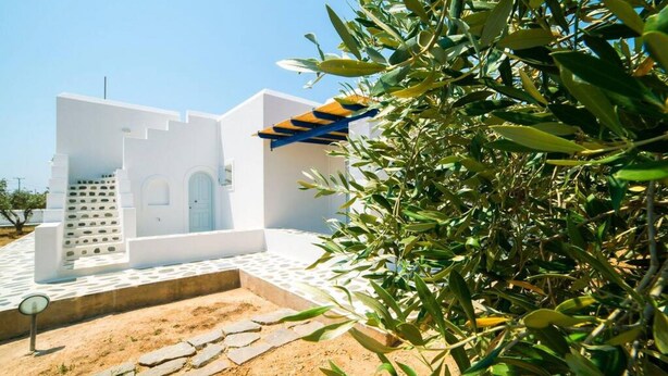 A white building with a blue and yellow awning, surrounded by olive trees and a clear sky. - Angel Villa in Paros (Lagkeri)