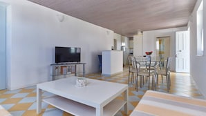 A modern living room with a flat-screen TV, a white coffee table, and a dining area with chairs and a table. - Angel Villa in Paros (Lagkeri)