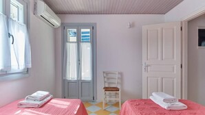 A room with two beds, a chair, a door, and an air conditioning unit. - Angel Villa in Paros (Lagkeri)