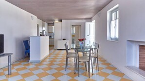 A spacious kitchen with a checkered floor, a dining area with a glass table and metal chairs, and a fireplace. - Angel Villa in Paros (Lagkeri)