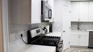 Una cocina moderna con armarios blancos, un microondas integrado, una estufa y un lavamanos.