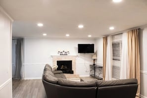 A living room with a fireplace, a sofa, and a television mounted on the wall. - Lovely 3-Bedroom Duplex (Douglasville)
