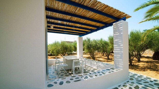 An outdoor patio with a table and chairs, surrounded by a white wall and a thatched roof. - Aegean Villa in Paros (Lagkeri)
