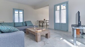 A modern living room with a grey sofa, a wooden coffee table, and a glass side table with a flat-screen TV. - Aegean Villa in Paros (Lagkeri)