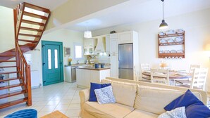Uma sala ampla com sofá, escada de madeira, cozinha com armários brancos e espaço de jantar com cadeiras e mesa.