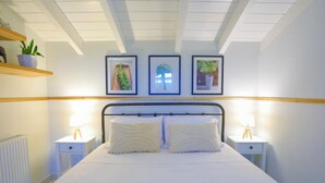 Cama bem arrumada com lençóis brancos, duas mesas de cabeceira com abajures e três quadros na parede.