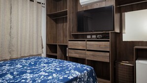 Un dormitorio con cama, televisor, estanterías de madera y un equipo de aire acondicionado.
