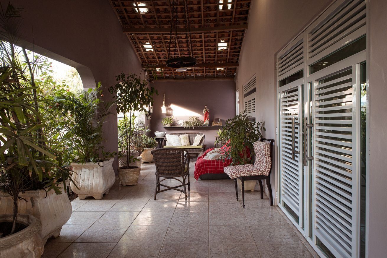 A covered patio area with potted plants, wicker furniture, and a statue.