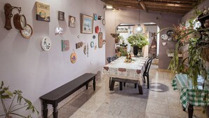 Un comedor con una mesa dispuesta para dos personas, rodeada de sillas. Hay un banco contra la pared y varios objetos decorativos colgados.