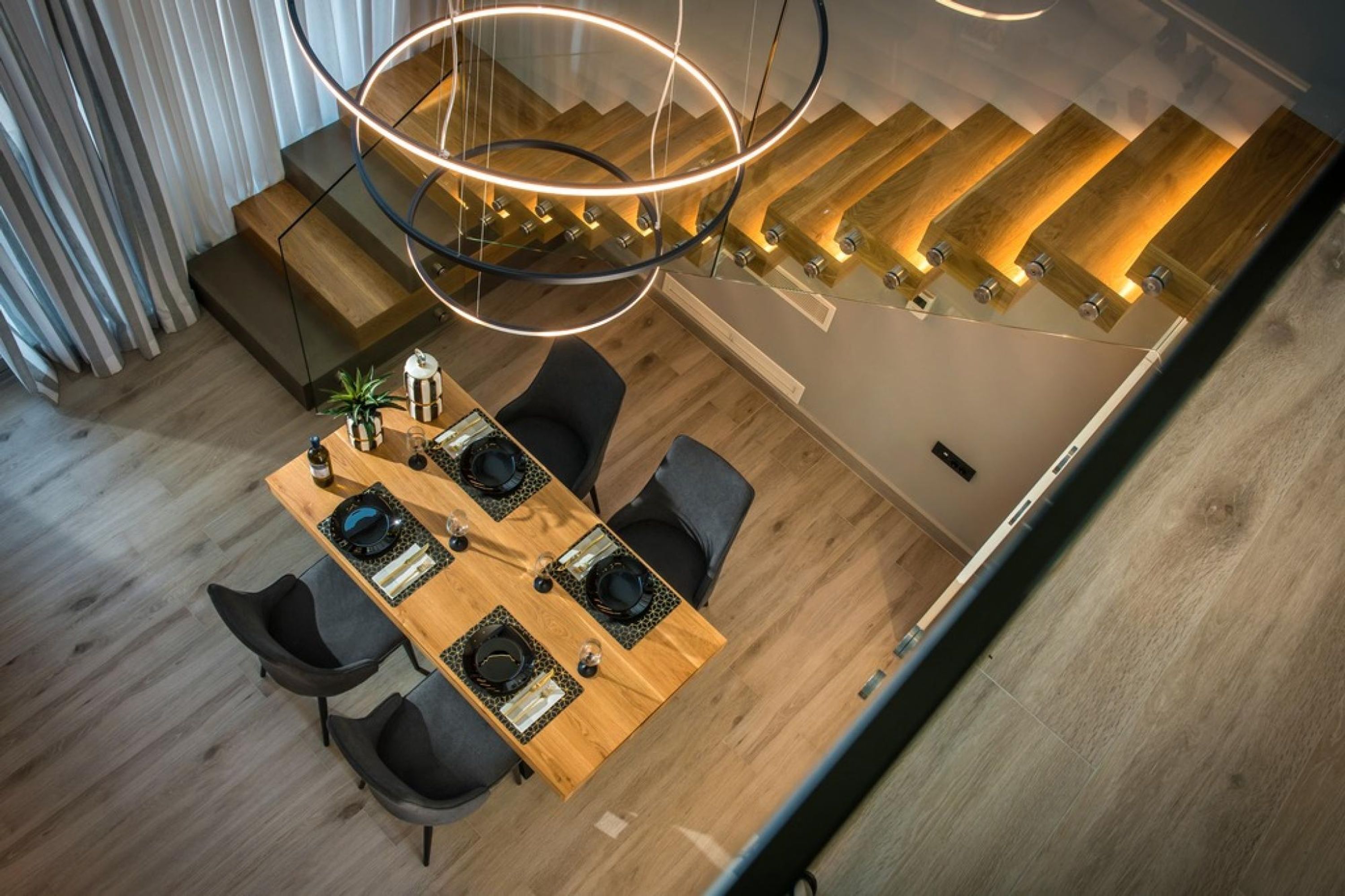 Un espace de salle à manger moderne avec une table en bois, des chaises noires et un luminaire circulaire original.