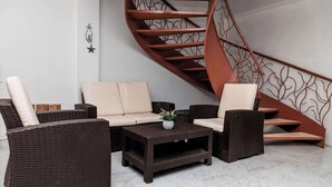 Ein moderner Wohnbereich mit einem braunen Rattansitzmöbel, einem kleinen Couchtisch und einer Wendeltreppe mit Metallgeländer.