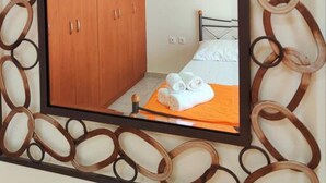 Un dormitorio con un armario de madera, una cama con colchón blanco y manta naranja, y un espejo con marco decorativo.