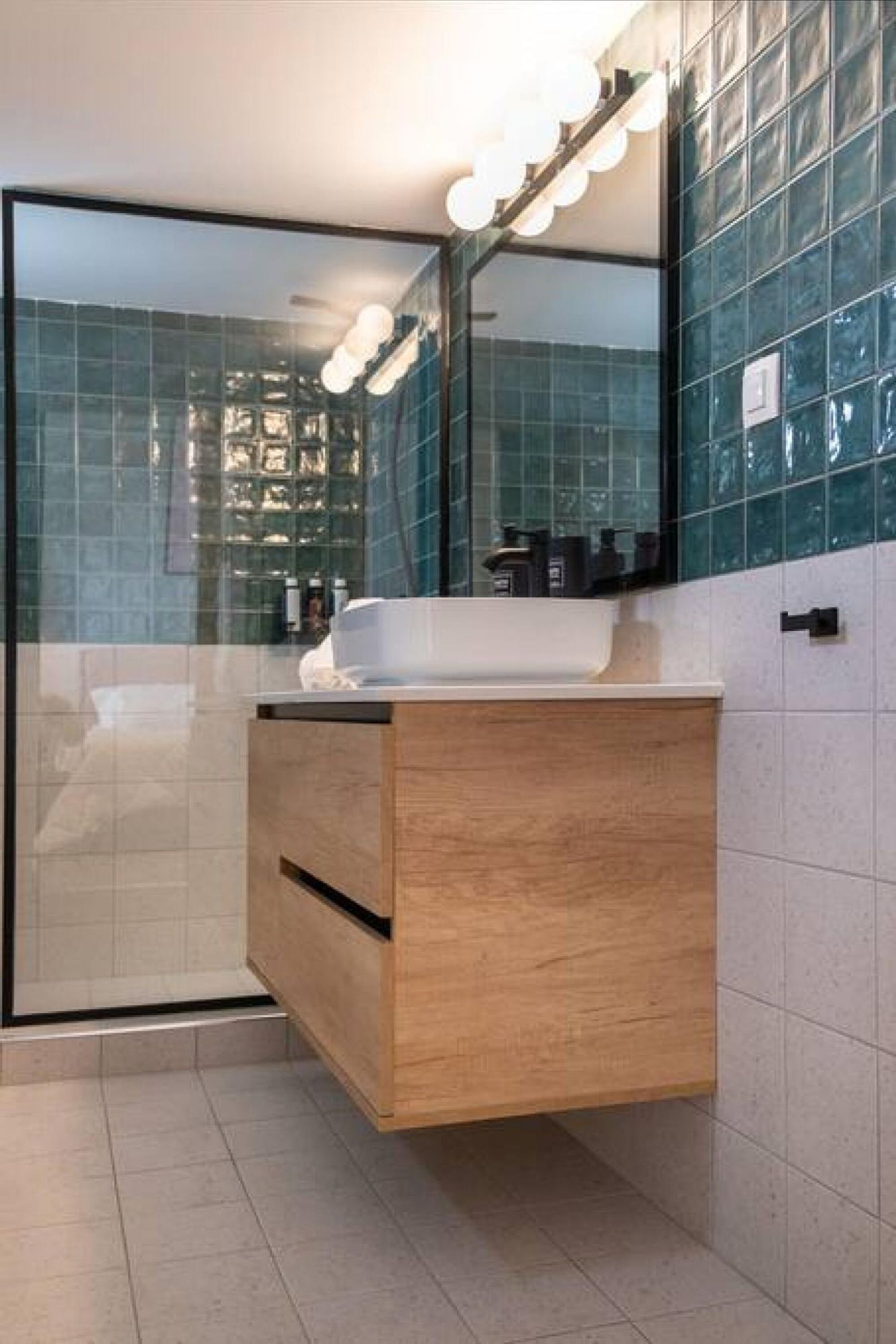 Een moderne badkamer met een douchecabine van glas, een houten wastafelmeubel en een spiegel met verlichting.