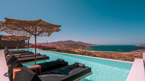 An infinity pool with lounge chairs and umbrellas overlooking a coastal landscape. - Sea la vie villa Private pool (MYKONOS)