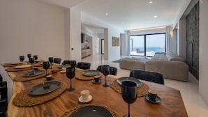 A modern dining area with a wooden table set for a meal, a sofa, and a stone accent wall. - Sea la vie villa Private pool (MYKONOS)