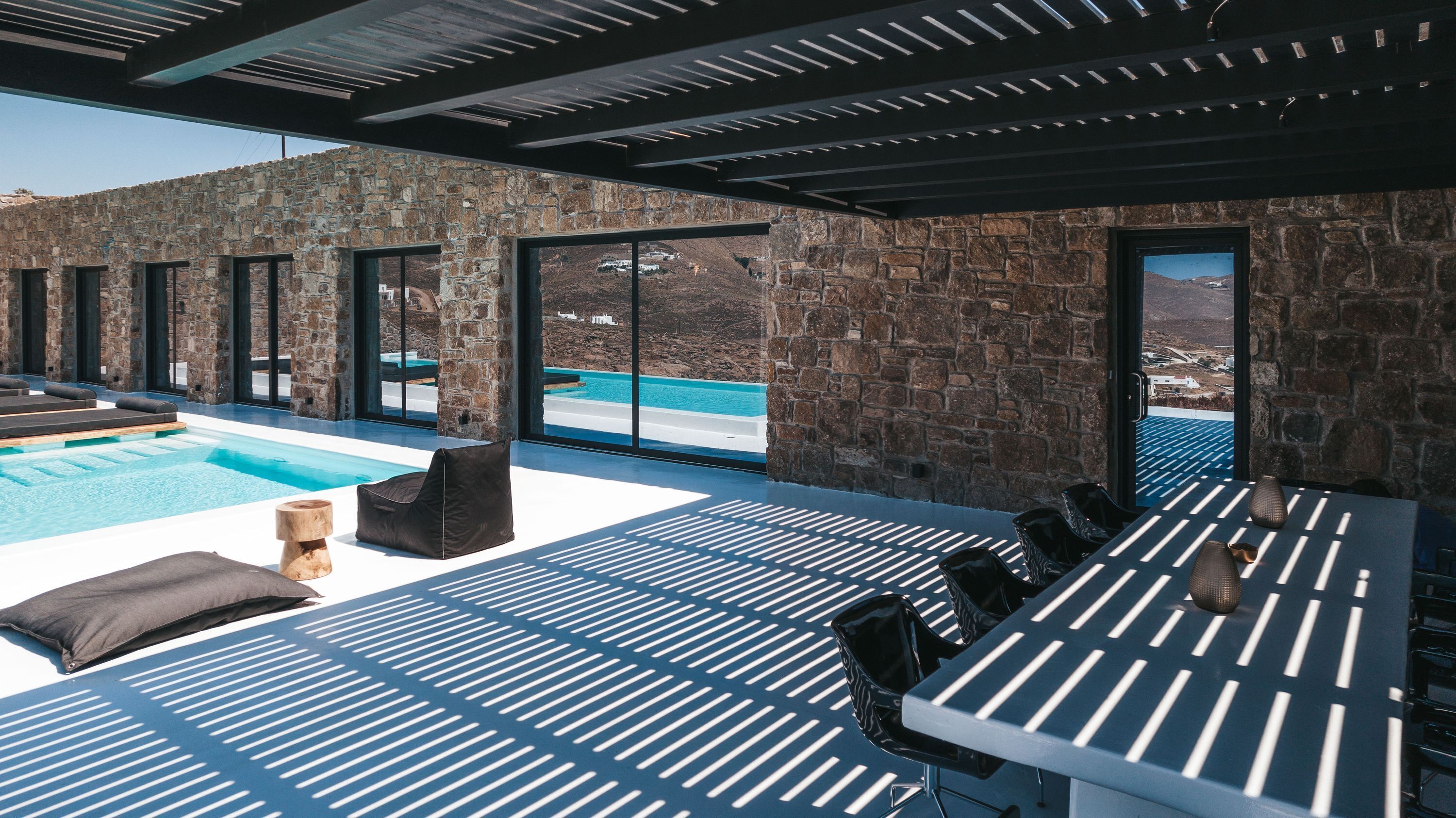 A modern outdoor pool area with stone walls and large windows, offering views of a mountainous landscape.