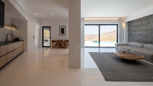 A modern living room with a large window, a stone wall, and a minimalist design. - Sea la vie villa Private pool (MYKONOS)