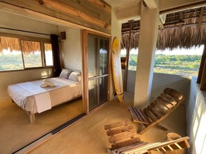 Une pièce avec un lit, une chaise en bois, une planche de surf et une vue sur le paysage.