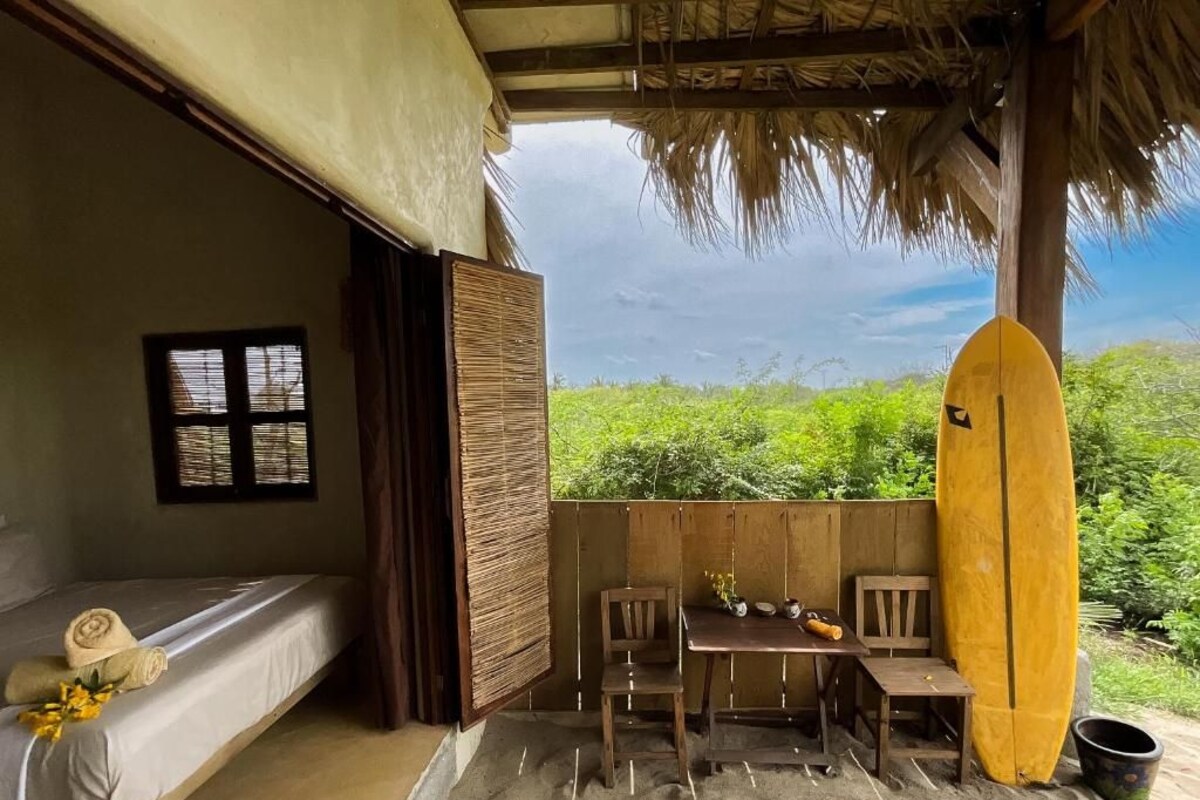 Une chambre avec un lit, une table, des chaises, une planche de surf et une vue sur la verdure.