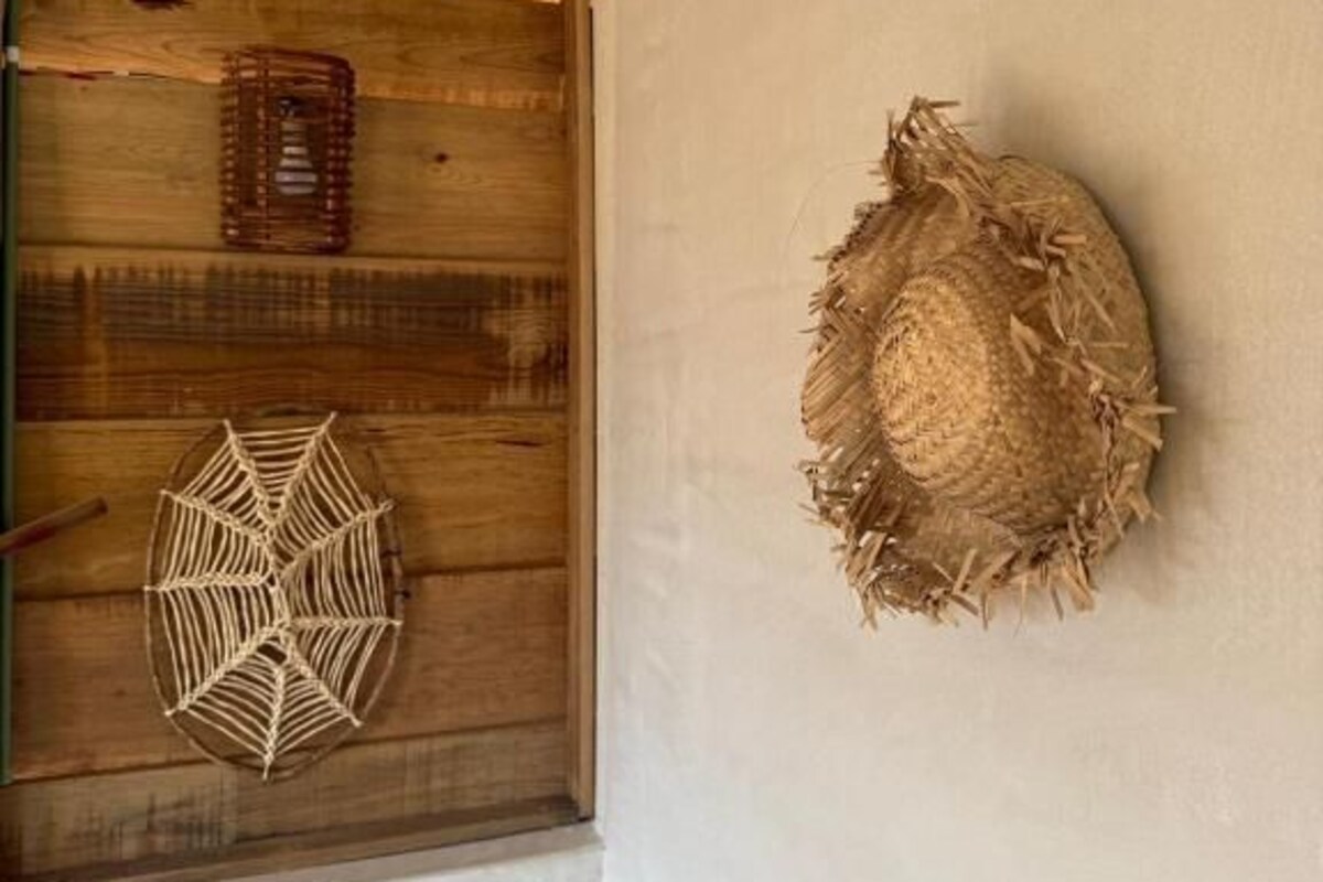 Une pièce avec un volet en bois à la fenêtre, un panier tressé et une décoration murale tissée.