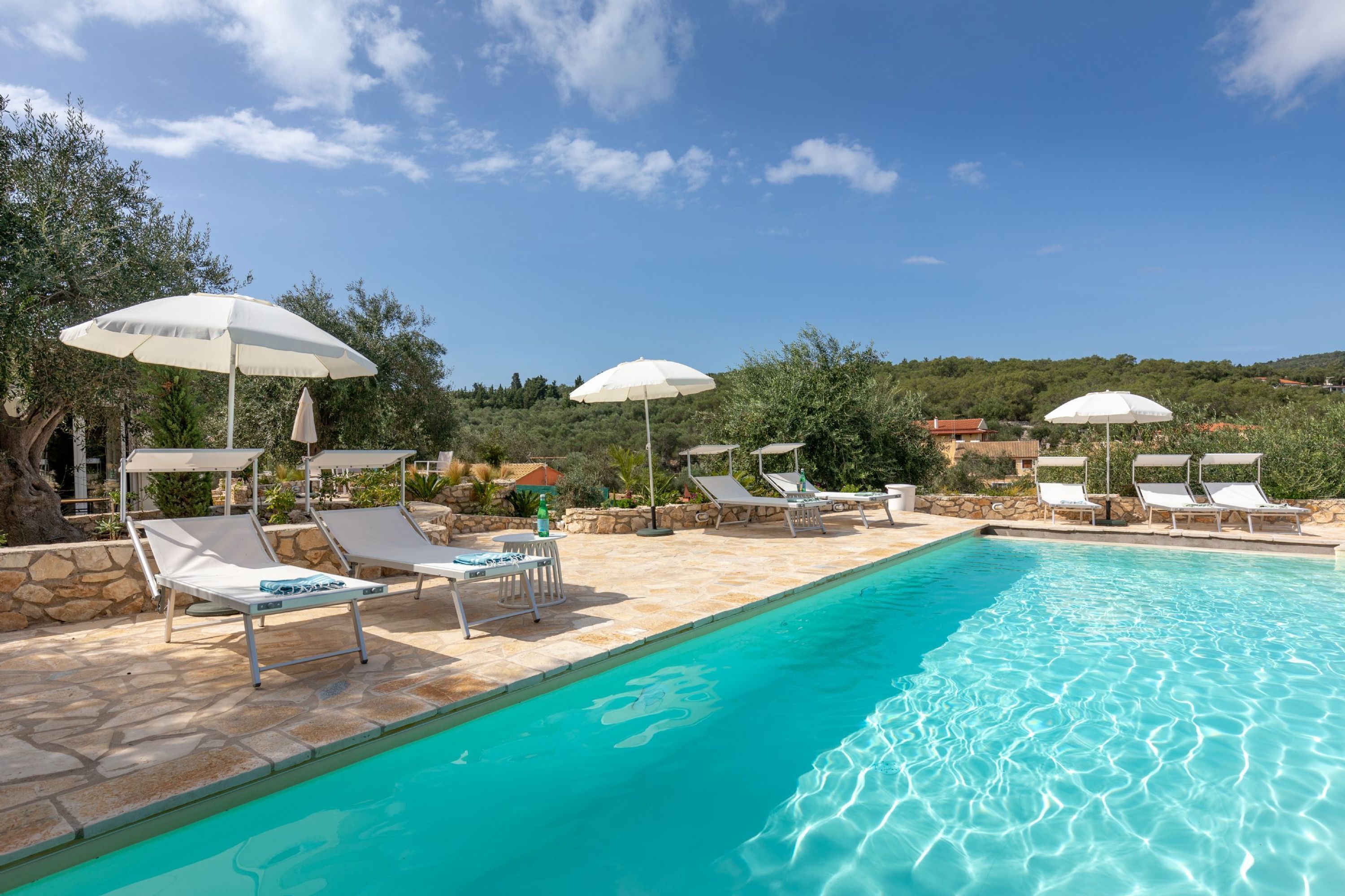 Un área junto a la piscina con sillones de descanso y sombrillas, una piscina azul cristalina y vistas del paisaje circundante.